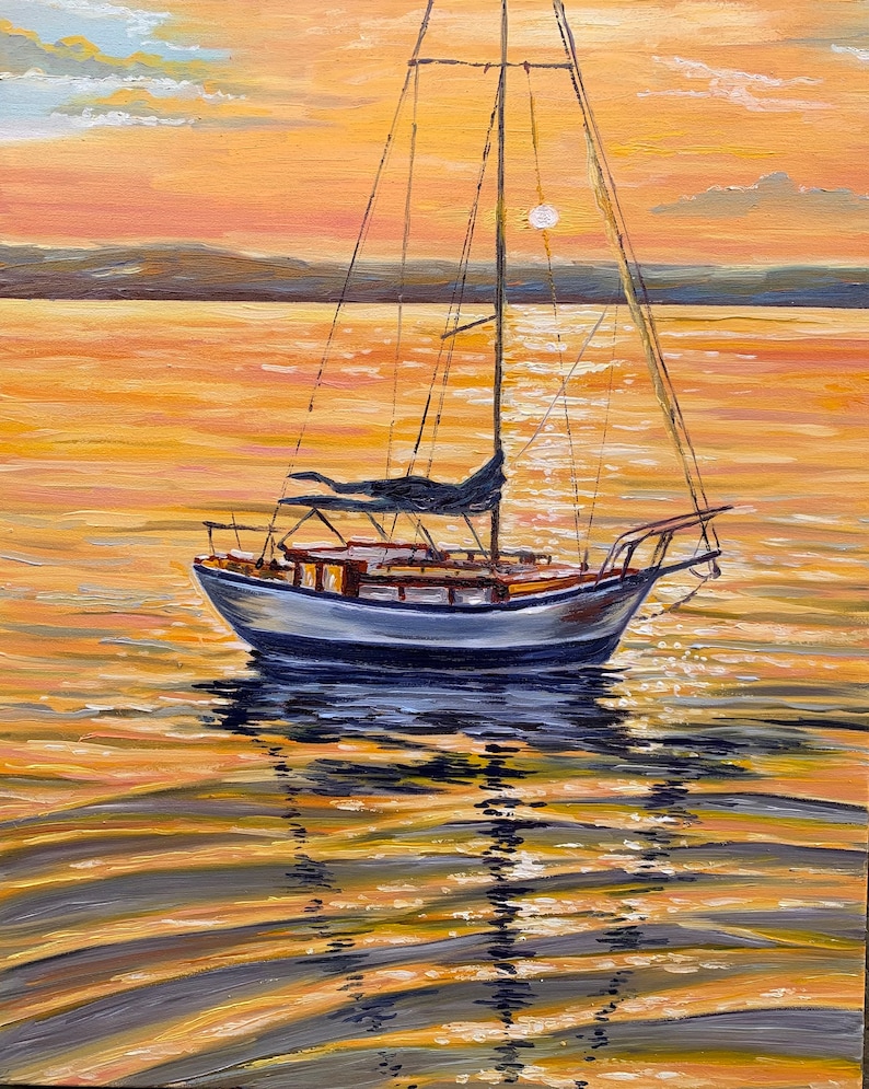 May include: A sailboat with a white hull and a dark blue sail is anchored in a calm body of water. The water is a golden color, reflecting the setting sun. The sky is a soft orange and pink.