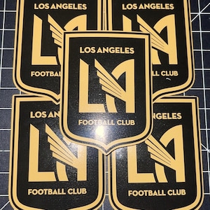 May include: Five black and gold stickers with the Los Angeles Football Club logo. The logo features a stylized "LA" with wings.