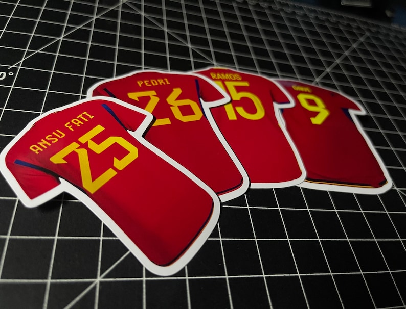 May include: Four red soccer jerseys with yellow numbers and player names. The jerseys have the numbers 25, 26, 15, and 9.