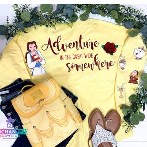 May include: Yellow sweatshirt with the text "Adventure in the great wide somewhere" in red glitter. The sweatshirt features a red rose, a teacup, and characters from the Disney movie Beauty and the Beast.