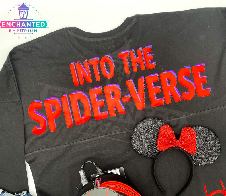 May include: Black long-sleeved shirt with the text "Into the Spider-Verse" in red with a purple outline. A black headband with a red glitter bow is in the bottom right corner.