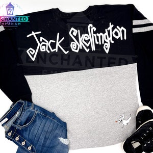 May include: Black and grey long-sleeved shirt with white lettering that says "Jack Skellington" and a white graphic of Jack Skellington on the bottom right side of the shirt.
