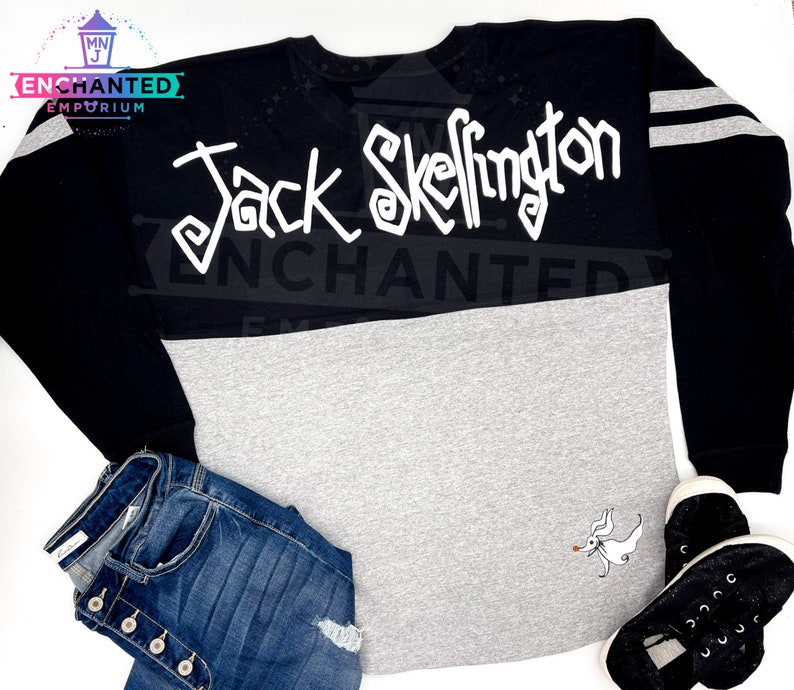 May include: Black and grey long-sleeved shirt with white lettering that says "Jack Skellington" and a white graphic of Jack Skellington on the bottom right side of the shirt.