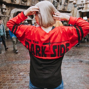 May include: Red and black long-sleeved shirt with the text "Join the Dark Side" in black glitter lettering. The shirt has black stripes on the sleeves.