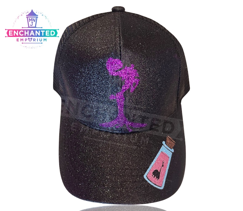 Op de afbeelding: Zwarte glitter trucker cap met een paars glitter ontwerp van een silhouet van een persoon die een fles vasthoudt. De fles heeft een roze vloeistof en een roze silhouet van een wezen erin.