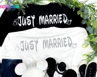 May include: Two white long-sleeved shirts with the text "Just Married" in silver glitter. The shirts are laid out on a white surface with Mickey Mouse ears and a crown.