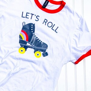 Peut inclure: T-shirt blanc avec un col rouge et un graphique de patin &agrave; roulettes avec le texte "Let's Roll".