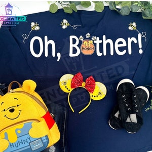 May include: A navy blue sweatshirt with the text "Oh, Bother!" in white. The sweatshirt has a small honey pot with bees and the text "Honey" on it. There is a Winnie the Pooh backpack and a pair of black shoes in the image.