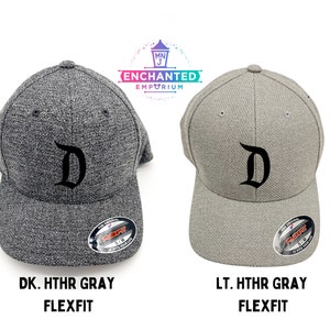 May include: Two baseball caps with a black stylized "D" on the front. The cap on the left is dark heather gray and the cap on the right is light heather gray. Both caps are Flexfit.
