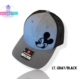 May include: A light gray and black baseball cap with a black Mickey Mouse silhouette on the front. The cap is a trucker style with a mesh back.