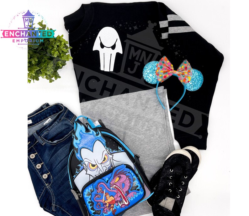 May include: Black sweatshirt with a white ghost graphic and the text "MNJ Enchanted" in white. A blue and pink bow headband, a pair of black sneakers, a pair of blue jeans, and a blue and black backpack with a Hades graphic.