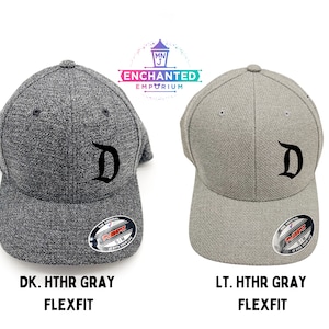 May include: Two baseball caps with a black "D" embroidered on the front. The cap on the left is dark heather gray and the cap on the right is light heather gray. Both caps have a Flexfit label on the back.