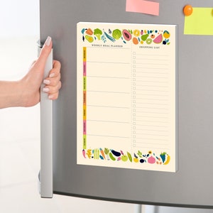May include: A white magnetic weekly meal planner and shopping list with a colorful border of fruits and vegetables. The planner has a column for each day of the week and a section for a shopping list.
