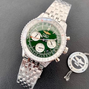 May include: A Breitling Navitimer chronograph watch with a green dial, three silver sub-dials, and a stainless steel link bracelet. The watch features a circular slide rule bezel, a date window, and a gold logo. A matching circular tag is included.
