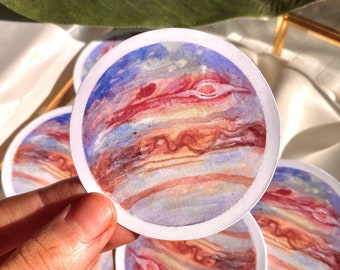 Könnte beinhalten: Ein Set mit vier runden Aufklebern mit einer Aquarellmalerei von Jupiter. Der Planet ist mit wirbelnden Bändern in Rot, Orange, Braun und Blau dargestellt.