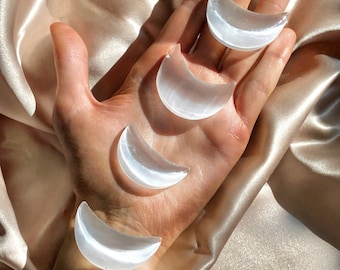 May include: Four white selenite crescent moon shaped crystals on a hand. The crystals are smooth and polished.