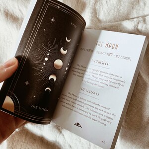 Puede incluir: Una gu&iacute;a de lectura de cartas de tarot con una ilustraci&oacute;n en negro y dorado de la luna. La carta se titula "La Luna" y describe el significado de la carta tanto en posici&oacute;n vertical como invertida. El texto incluye las palabras "enga&ntilde;o, inseguridad, ilusi&oacute;n".