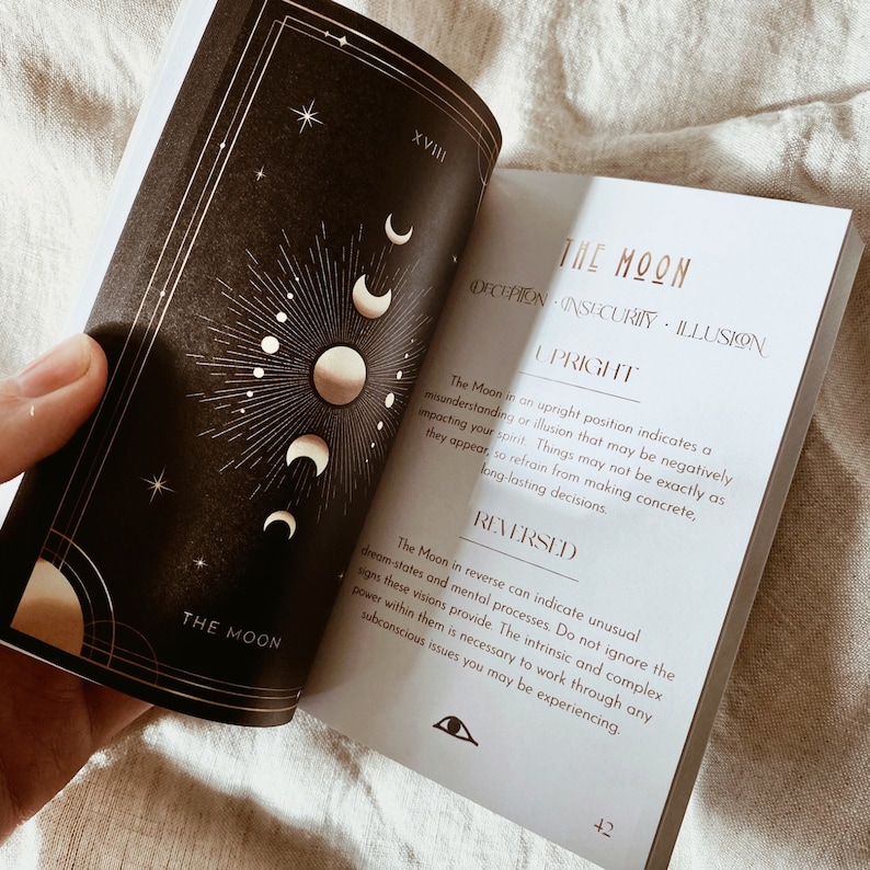 Puede incluir: Una gu&iacute;a de lectura de cartas de tarot con una ilustraci&oacute;n en negro y dorado de la luna. La carta se titula "La Luna" y describe el significado de la carta tanto en posici&oacute;n vertical como invertida. El texto incluye las palabras "enga&ntilde;o, inseguridad, ilusi&oacute;n".