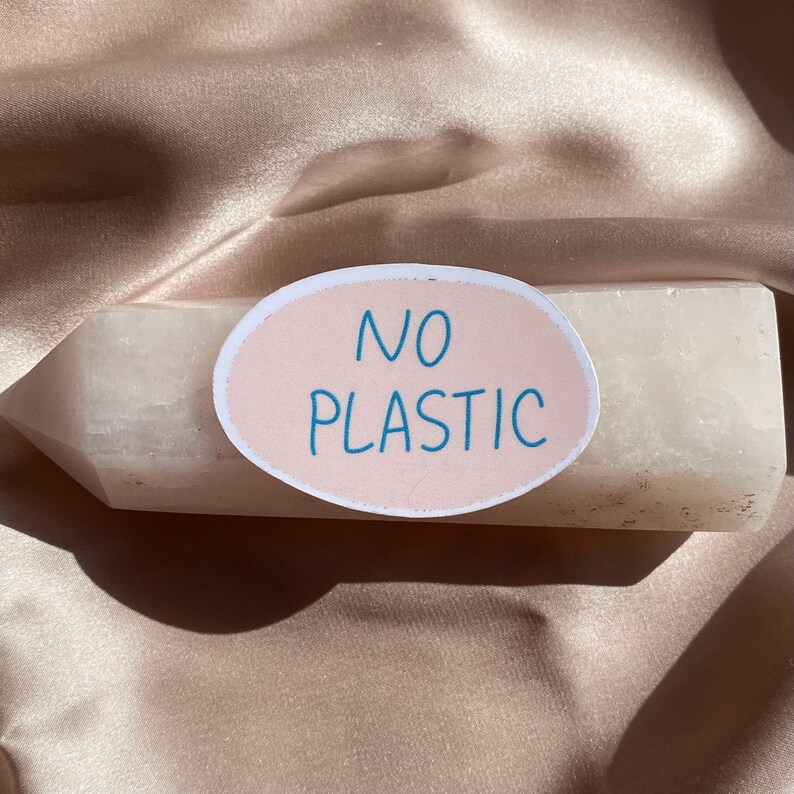 May include: A light-colored crystal with an oval sticker that reads "NO PLASTIC" in blue text. The crystal is resting on a satin fabric.