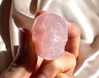May include: A pink rose quartz crystal skull. The skull is carved in detail and has a smooth, polished finish.