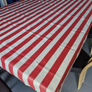 Peut inclure: Une nappe à rayures rouges et blanches recouvre une table. Les rayures sont larges et espacées uniformément, créant un motif audacieux. La nappe est en matière lisse. La table est rectangulaire.
