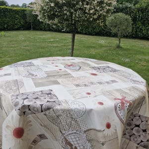 May include: A round tablecloth with a light wood grain pattern, featuring floral and heart motifs. The word "NATURE" is spelled out in wooden block letters. The tablecloth is set on a green lawn with trees in the background.