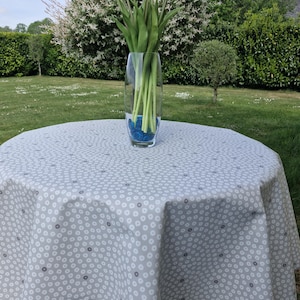 Pode incluir: Uma toalha de mesa redonda cinza claro com um padrão de pontos brancos e cinza escuro cobre uma mesa. Um vaso de vidro transparente cheio de tulipas coloridas e contas decorativas azuis está sobre a mesa, com um gramado verde e folhagem ao fundo.