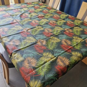 Puede incluir: Un mantel negro con un patrón de hojas tropicales en tonos de verde, amarillo y rojo. El mantel está puesto sobre una mesa de madera con sillas.