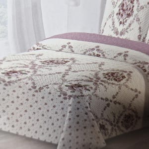 Peut inclure: Une couette blanche et rose à motifs floraux avec un design matelassé. La couette est pliée sur un lit avec un oreiller à motifs floraux blancs et roses.