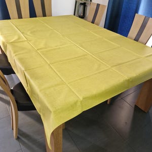 Könnte beinhalten: Eine gelbe Tischdecke mit subtiler Textur, die einen Esstisch aus Holz mit vier Stühlen bedeckt. Die Tischdecke ist über den Tisch gelegt und hängt an allen Seiten herunter.