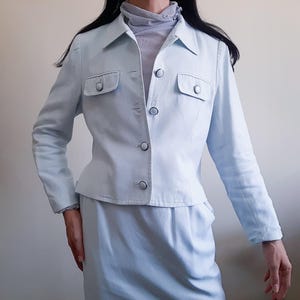 K&ouml;nnte beinhalten: Hellblauer zweiteiliger Anzug. Die Jacke hat zwei Vordertaschen, einen Kragen und Kn&ouml;pfe. Der Rock hat die passende hellblaue Farbe. Der Anzug ist aus einem weichen Stoff gefertigt.
