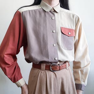 Op de afbeelding: Een overhemd met lange mouwen en knoopsluiting in een color-block ontwerp met tinten terracotta, taupe en crème. Het overhemd heeft een borstzak met een terracotta flap, een puntige kraag en bijpassende knopen, gecombineerd met een bruine leren riem.