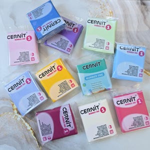 Peut inclure: Plusieurs paquets de pâte polymère Cernit de différentes couleurs, rose, bleu, jaune et vert. Chaque paquet porte l'inscription "Cernit Number One" et contient des informations sur le produit. Idéal pour le modelage et la sculpture.