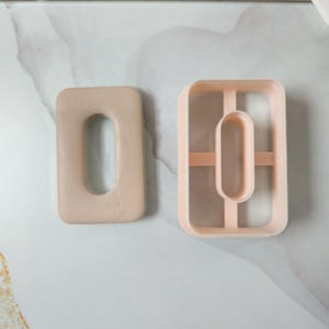 Può includere: Due formine per biscotti color pesca chiaro. Una è un rettangolo pieno con un ritaglio ovale dai bordi arrotondati. L'altra è un telaio rettangolare con un ritaglio ovale al centro. Entrambi sono in plastica.