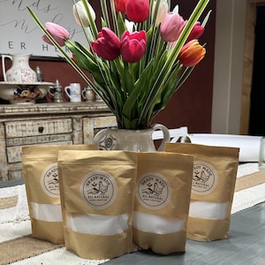 May include: A display featuring a vase of vibrant tulips in shades of red, pink, and orange, with green foliage. In front, there are four kraft paper pouches with a clear window and a label that reads "BRADY MADE ALL NATURAL HAND CRAFTED".