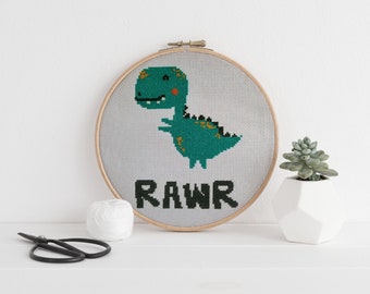 May include: A green dinosaur cross-stitch pattern in a wooden embroidery hoop with the word "RAWR" underneath.