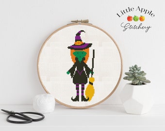 May include: A cross-stitch pattern of a green witch with a purple hat and broom, framed in a wooden hoop. The pattern is titled "Little Apple Stitchery".