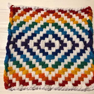 May include: A rainbow-colored woven pot holder with a white background. The pot holder is made of thick cotton yarn and has a checkered pattern.