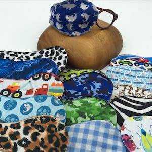 May include: Assortment of colorful eye patches with various patterns, including sharks, trucks, camouflage, and animals. The patches are made of soft fabric and have a curved shape.