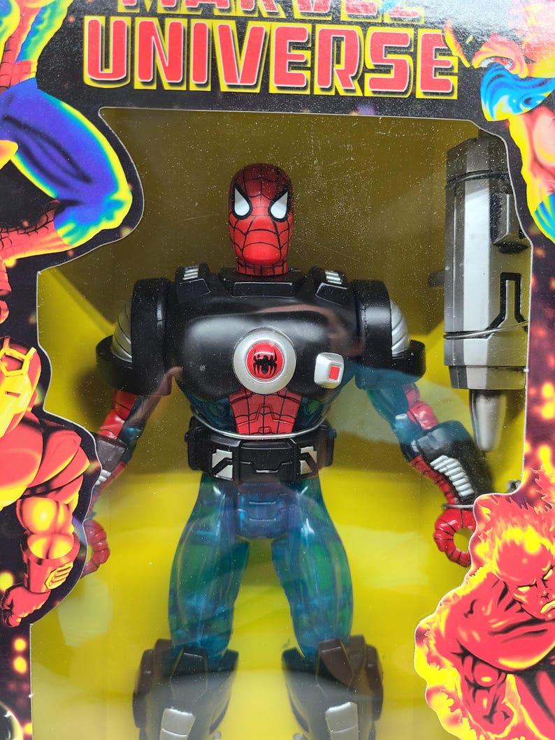 Puede incluir: Una figura de acci&oacute;n roja y negra de Spider-Man con un traje de armadura negro y plateado. La figura sostiene un arma plateada y est&aacute; de pie sobre un fondo amarillo. La figura es parte de la l&iacute;nea de juguetes Marvel Universe.