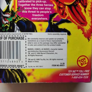 Puede incluir: Una caja roja, amarilla y azul con una imagen de una figura humana roja rodeada de llamas. La caja es para una figura de acci&oacute;n de Marvel Comics. El texto en la caja dice "Toy Biz" y "Armor Spider-Man".