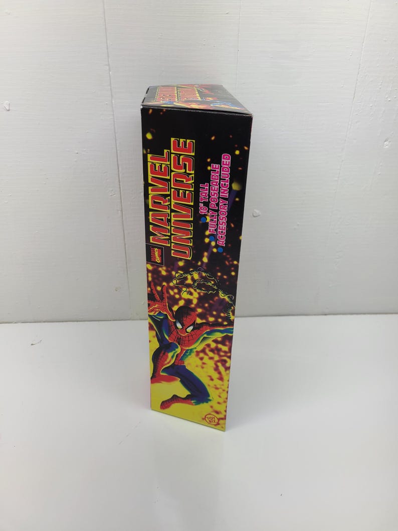 Puede incluir: Una caja negra con una imagen roja y amarilla de Spider-Man en el lateral. La caja dice "Marvel Universe" y "10" tall fully poseable accessory included."
