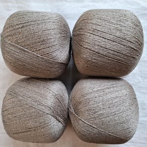 Op de afbeelding: Vier ronde bollen lichtbruin garen gerangschikt in een vierkante formatie. Elke bol heeft een strak gewonden, gladde textuur met zichtbare individuele vezelstrengen, wat een consistente neutrale aardetint door de hele set laat zien.