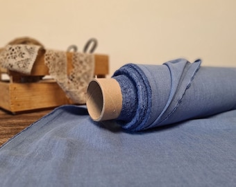 May include: A roll of light blue fabric with a cardboard core. The fabric is unraveled at the end, showing its texture. A wooden crate with lace and scissors is in the background.