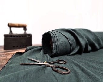 May include: A roll of dark teal fabric with a pair of vintage scissors and an antique iron. The fabric is unrolled on a wooden surface, with the iron in the background. The scissors are open, ready for use.