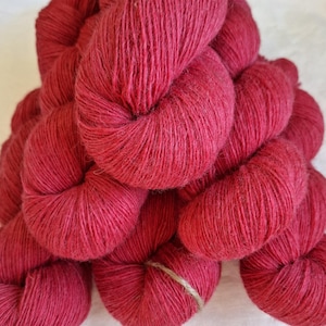 Puede incluir: Primer plano de varios ovillos de hilo rojo vibrante. El hilo está enrollado firmemente en paquetes ordenados, con una cuerda de fibra natural que asegura uno de los ovillos. La textura del hilo parece suave y ligeramente borrosa, ideal para proyectos de tejido o ganchillo.