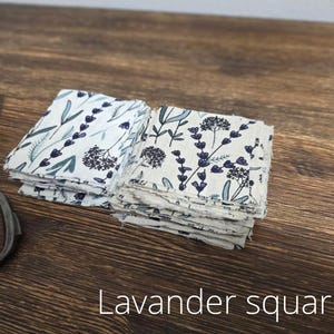 May include: Two stacks of square fabric pieces with a floral lavender pattern in blue and green on a white background. A pair of vintage scissors is on the left. The text "Lavender squares" is at the bottom.