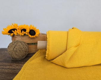 May include: A roll of yellow linen fabric with a brown cardboard core. The fabric is folded and draped over a wooden surface. A small bouquet of sunflowers is in the background.