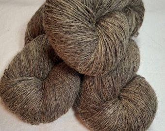 May include: Close-up of several skeins of brown yarn. The yarn is a mix of light and dark brown fibers, creating a textured appearance. The yarn is tightly wound into round shapes, suggesting it is ready for use in knitting or crocheting projects.