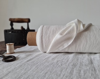 May include: A white linen fabric roll, folded and displayed on a white linen surface. A spool of thread and a pair of scissors are also visible in the image.